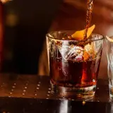 Ein dunkler Whisky wird in ein Glas mit Eis und Orangenzeste gegossen. So trinkt man Whisky.