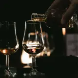 Ein Glas wird mit bernsteinfarbenem Brandy oder Cognac gefüllt, während andere Gläser bereitstehen.