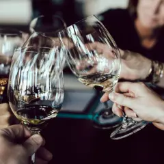 Hände halten Weingläser am Stiel, um den Wein richtig zu halten. Ein Toast wird ausgesprochen.