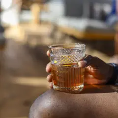 Ein Mann hält ein Glas Wermut mit Eis und Orangenzeste. So trinkt man Wermut an einem sonnigen Tag.