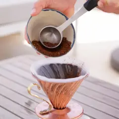 Eine Hand schüttet frisch gemahlenen Kaffee aus einer Schale in einen Kupfer-Filterhalter. So wird der perfekte Kaffee gekocht.