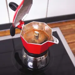 Rote Mokkakanne auf schwarzer Kochplatte, die frisch gebrühten Mokka Kaffee produziert.