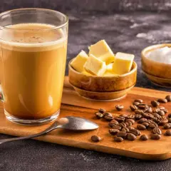 Ein Glas cremiger Kaffee, daneben Butterwürfel und Kokosöl. So wird Bulletproof Coffee zubereitet.