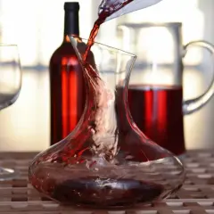 Roter Wein wird in eine Karaffe gegossen, ein Beispiel für Dekantieren. Daneben stehen ein Weinglas und eine weitere Karaffe mit Wein.