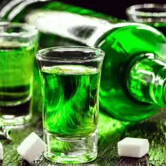 Grüner Branntwein aus Wermut, serviert in Schnapsgläsern mit Zuckerwürfeln und Limettenspalten.