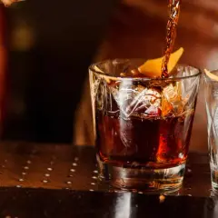 Ein dunkler Whisky wird in ein Glas mit Eis und Orangenzeste gegossen. So trinkt man Whisky.