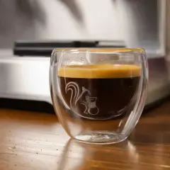 Ein dampfendes Espresso am Abend in einem doppelwandigen Glas mit einem süßen Eichhörnchen-Motiv. Perfekt für gemütliche Stunden.
