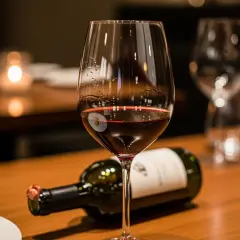Ein Glas Rotwein mit leichtem Bodensatz beim Wein steht neben einer liegenden Flasche auf einem Holztisch.