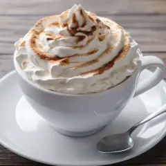 Ein cremiger Kapuziner Kaffee, üppig garniert mit Schlagsahne und Zimt, wartet auf einem Holztisch.