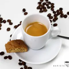 Ein cremiger Espresso Lungo in weißer Tasse, daneben ein Cantuccini und Kaffeebohnen.