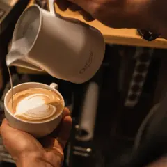 Barista verziert einen Kaffee mit kunstvoller cafe latte art. Ein Herz aus Milchschaum entsteht.