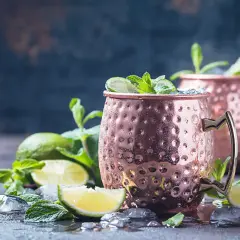 Zwei eisgekühlte Moscow Mule Becher mit Limette und Minze. Die Herkunft des Moscow Mule ist eine interessante Geschichte.