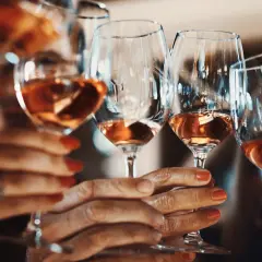 Hände halten Gläser mit Roséwein. Die Frage, warum Sulfite im Wein sind, beschäftigt viele Genießer.