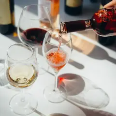 Roséwein wird in ein Glas gegossen, während Weiß- und Rotwein bereits in anderen Gläsern stehen. Ein schöner Moment, um Wein zu servieren.