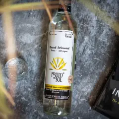Flasche Mezcal "Fruto del Sol" neben einem Glas und Büchern. So trinkt man Mezcal: pur und langsam genießen.