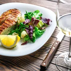 Gegrilltes Lachsfilet mit Salat und Zitrone, dazu ein Glas Weißwein, der den Riesling Geschmack unterstreicht.