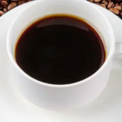 Eine Tasse schwarzer Kaffee umgeben von gerösteten Kaffeebohnen. Die Frage "wie viel Koffein hat Kaffee?" wird durch dieses Bild aufgeworfen.