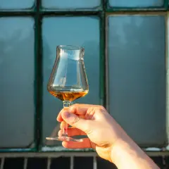 Hand hält ein Glas mit bernsteinfarbenem Whisky. Der Alkoholgehalt des Whiskys wird durch die Farbe und Klarheit angedeutet.