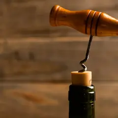 Ein Holzkorkenzieher mit Metallspirale wird in einen Korken gedreht. So funktioniert ein Korkenzieher: Drehen, bis die Spirale greift, dann ziehen.