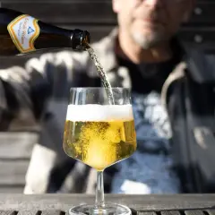 Ein Mann gießt ein Kristall-Weizenbier in ein Glas. Die Flasche zeigt "0,33l". Wenige Kalorien für diesen Genuss.