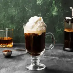 Ein Irish Coffee Rezept: Heißer Kaffee, Whiskey und Sahne in einem Glas, daneben eine French Press und ein Glas Whiskey.