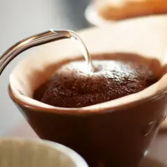 Heißes Wasser fließt aus einer schmalen Kanne auf frisch gemahlenen Kaffee in einem Filter. Der Prozess des Kaffee filterns beginnt.