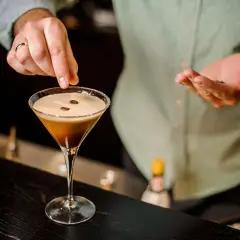Ein Barkeeper garniert einen Espresso-Martini mit Kaffeebohnen. Dieser Kaffee Cocktail ist ein Genuss.