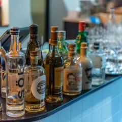 Eine Auswahl an Flaschen, darunter eine blaue Heidelbeer-Wodka-Flasche, steht auf einer Bar. Was ist Wodka? Eine klare Spirituose, oft aus Getreide oder Kartoffeln hergestellt.