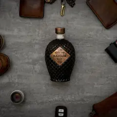 Edle Flasche Saigon Baigur Gin mit 43% Alkohol, umgeben von Lederaccessoires und einer Leica Kamera.