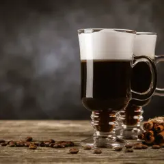 Zwei Irish Coffee Gläser mit Sahnehaube, Kaffeebohnen und Zimtstangen. Perfekt für Irish Coffee Rezepte.