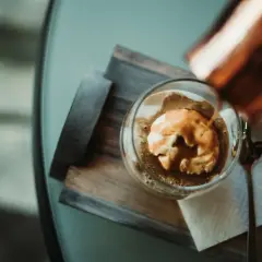 Ein Affogato: heißer Espresso fließt über eine Kugel cremiges cafe eis. Ein Löffel liegt daneben.