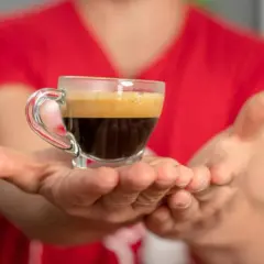 Hände reichen eine kleine Tasse Espresso, bereit für einen belebenden Kaffee-Nap.