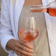 Eine Person schenkt Roséwein mit Eiswürfeln in ein Glas. Die ideale rosewein temperatur für diesen erfrischenden Genuss.