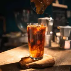 Ein erfrischender Eis Americano wird zubereitet, während Espresso in das Glas mit Eis und Wasser gegossen wird.