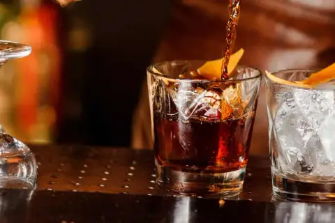 Ein dunkler Whisky wird in ein Glas mit Eis und Orangenzeste gegossen. So trinkt man Whisky.