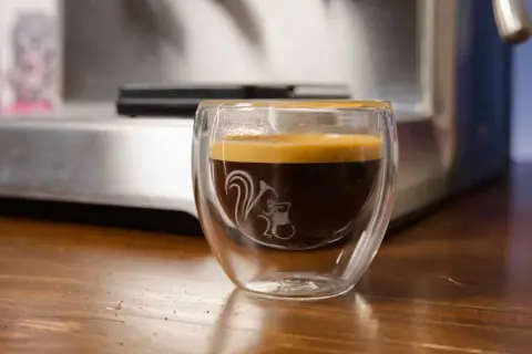 Ein dampfendes Espresso am Abend in einem doppelwandigen Glas mit einem süßen Eichhörnchen-Motiv. Perfekt für gemütliche Stunden.