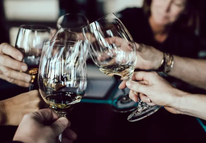 Hände halten Weingläser am Stiel, um den Wein richtig zu halten. Ein Toast wird ausgesprochen.
