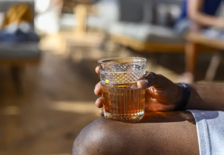 Ein Mann hält ein Glas Wermut mit Eis und Orangenzeste. So trinkt man Wermut an einem sonnigen Tag.