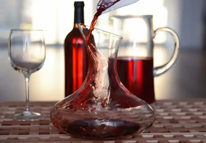 Roter Wein wird in eine Karaffe gegossen, ein Beispiel für Dekantieren. Daneben stehen ein Weinglas und eine weitere Karaffe mit Wein.