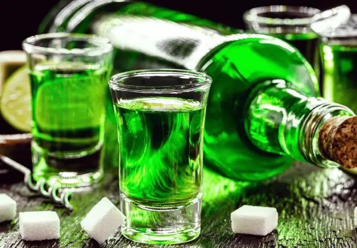 Grüner Branntwein aus Wermut, serviert in Schnapsgläsern mit Zuckerwürfeln und Limettenspalten.