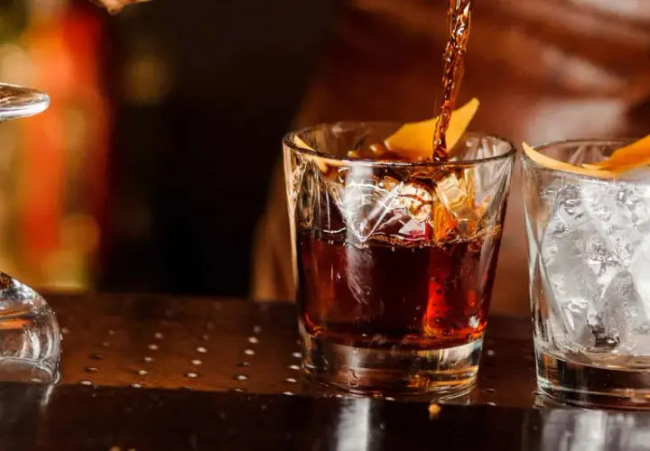 Ein dunkler Whisky wird in ein Glas mit Eis und Orangenzeste gegossen. So trinkt man Whisky.