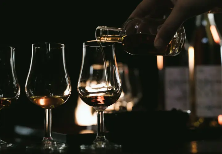 Ein Glas wird mit bernsteinfarbenem Brandy oder Cognac gefüllt, während andere Gläser bereitstehen.