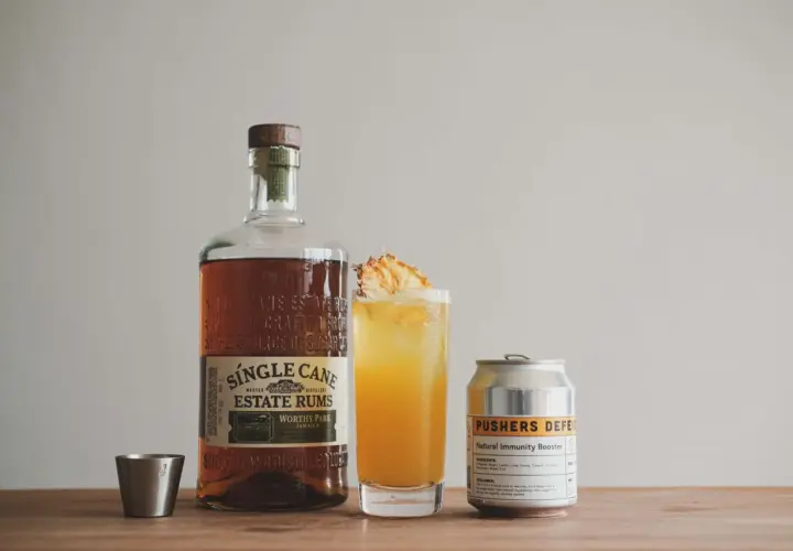 Flasche Single Cane Estate Rums, ein Cocktail mit Ananas und eine Dose "Pushers Defense". Der Rum hat seine Herkunft auf Jamaika.