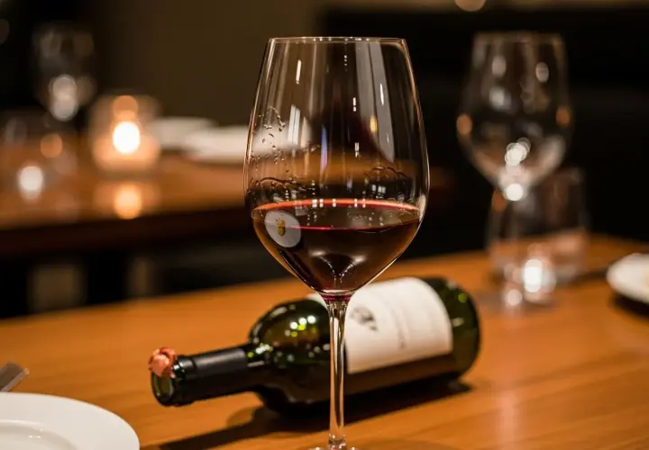 Ein Glas Rotwein mit leichtem Bodensatz beim Wein steht neben einer liegenden Flasche auf einem Holztisch.