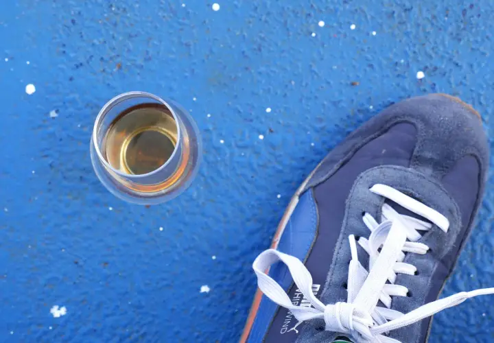 Ein Glas Whisky steht neben einem blauen Sneaker. Wer sich fragt, wie viel Kalorien hat Whisky, findet hier eine visuelle Anregung.
