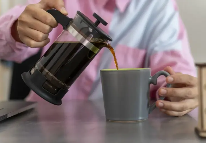 Kaffee wird aus einer French Press in eine graue Tasse gegossen.