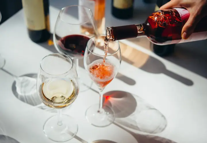 Roséwein wird in ein Glas gegossen, während Weiß- und Rotwein bereits in anderen Gläsern stehen. Ein schöner Moment, um Wein zu servieren.