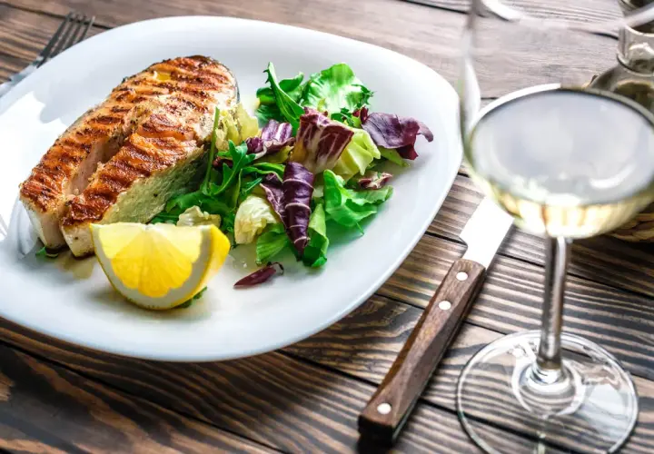 Gegrilltes Lachsfilet mit Salat und Zitrone, dazu ein Glas Weißwein, der den Riesling Geschmack unterstreicht.