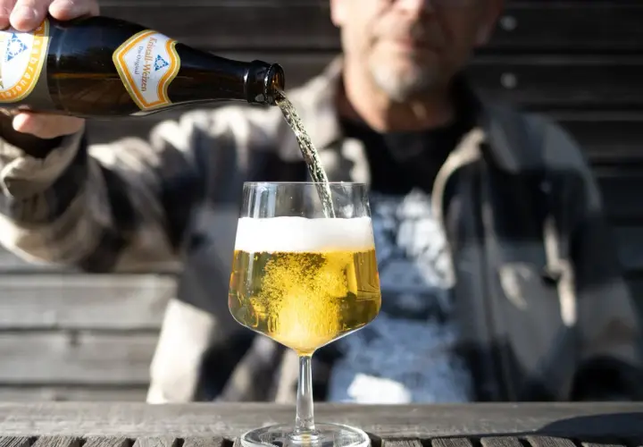 Ein Mann gießt ein Kristall-Weizenbier in ein Glas. Die Flasche zeigt "0,33l". Wenige Kalorien für diesen Genuss.
