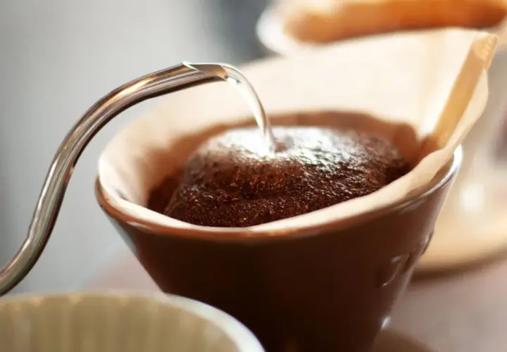 Heißes Wasser fließt aus einer schmalen Kanne auf frisch gemahlenen Kaffee in einem Filter. Der Prozess des Kaffee filterns beginnt.